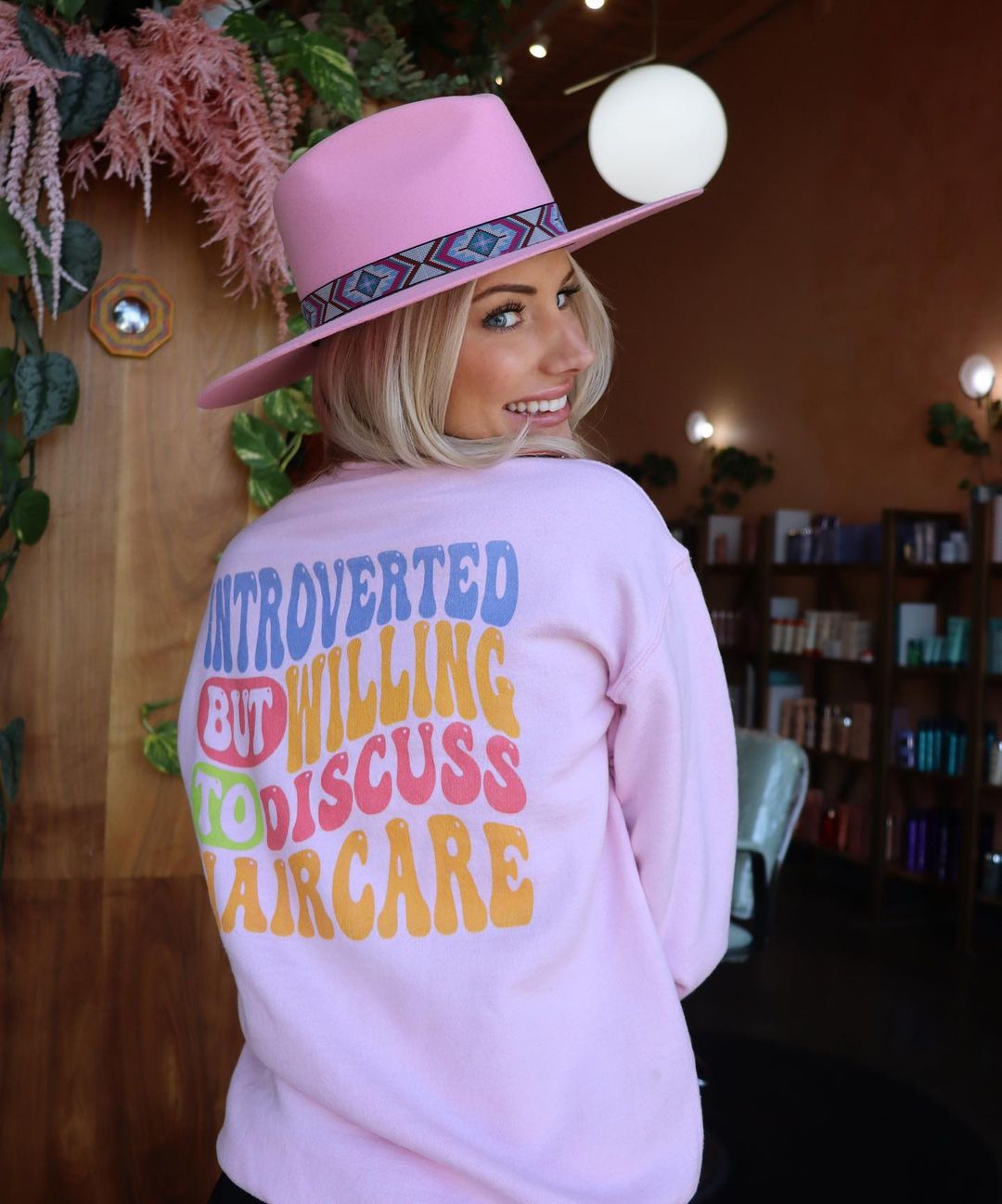 hairstylist in salon wearing a pink hat and a ready to dye apparel hairdresser sweater sweatshirt